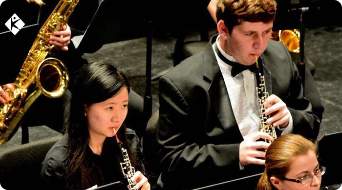 Sasha performing oboe alongside student musician in university wind ensemble rehearsal