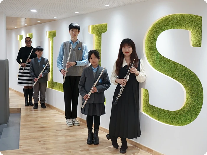 KLIS ensemble director Sasha with students holding flutes and oboe in school hallway